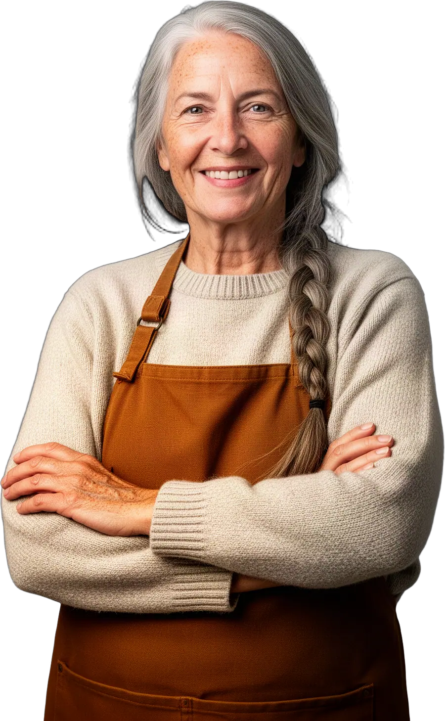 Smiling woman with long grey hair in a braid, oatmeal sweater and brown canvas apron, arms crossed